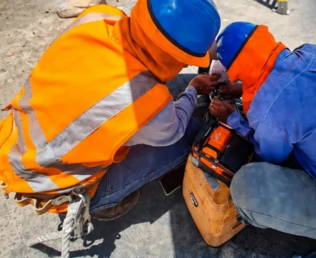 Dos técnicos con casco y chaleco naranja fusionan fibra óptica con una empalmadora