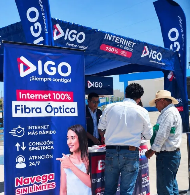Stand de Digo Telecom con banderas y banners, un asesor atiende a dos vecinos