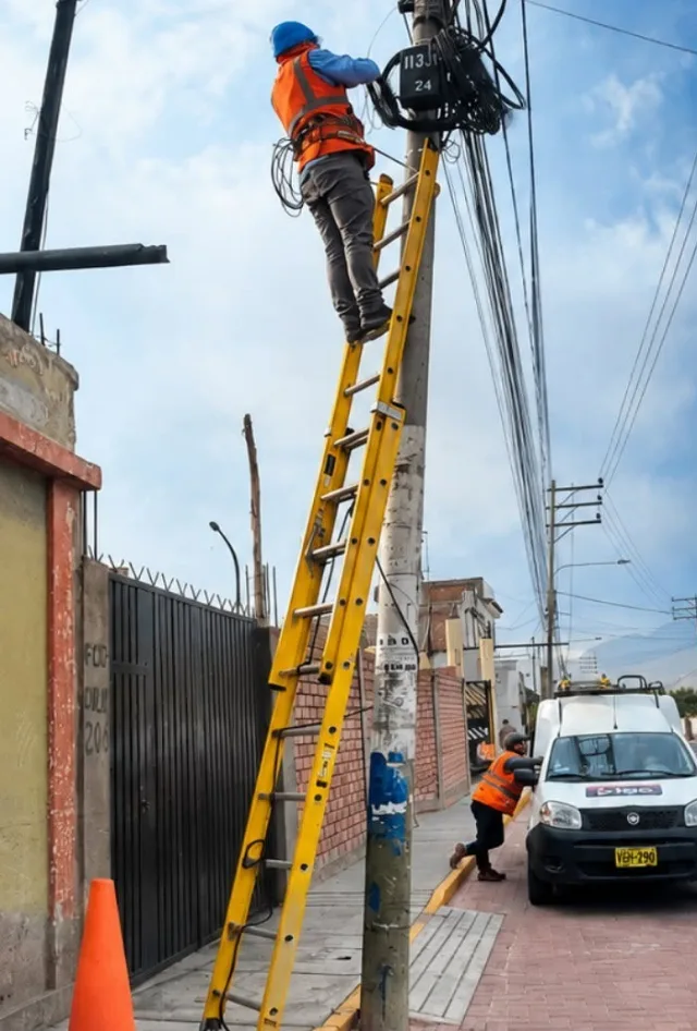 Técnico de Digo sobre una escalera trabajando en la caja de fibra de un poste; abajo, otro técnico junto a la camioneta de Digo